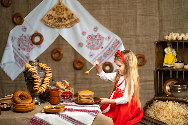 Shrovedite를 축하하는 동안 민속 의상 스프링클러 팬케이크에 꿀을 넣은 백인 소녀