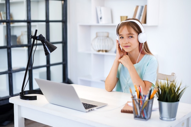 Little caucasian girl in headphones have video call distant class with teacher at home