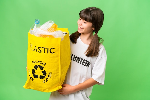 幸せな表情で孤立した背景にリサイクルするプラスチック ボトルの完全な袋を保持している白人少女