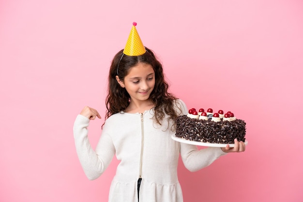 勝利を祝うピンクの背景に分離されたバースデーケーキを保持している小さな白人の女の子