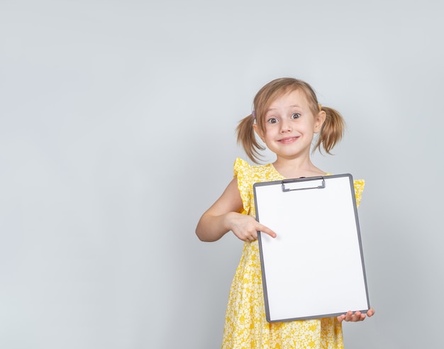 Little Caucasian girl holding a clipboard with a blank paper