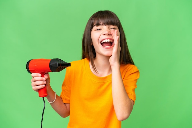 Little Caucasian girl holding a hairdryer over isolated background shouting with mouth wide open