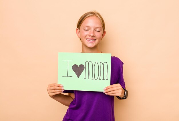 Little caucasian girl holding i love mom placard isolated on\
beige background