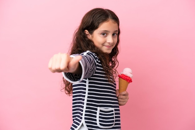 Little caucasian girl holding an ice cream isolated on pink background giving a thumbs up gesture