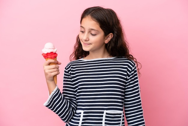 Little caucasian girl holding an ice cream isolated on pink background looking side