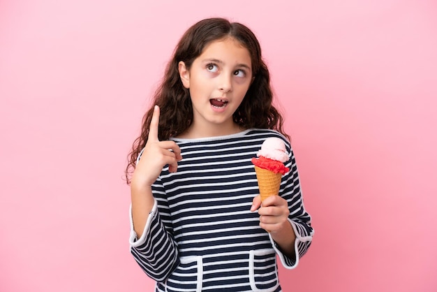 분홍색 배경에 격리된 아이스크림을 들고 손가락을 가리키는 아이디어를 생각하는 백인 소녀