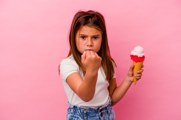 Little caucasian girl holding ice cream isolated on pink showing fist to camera, aggressive facial expression.