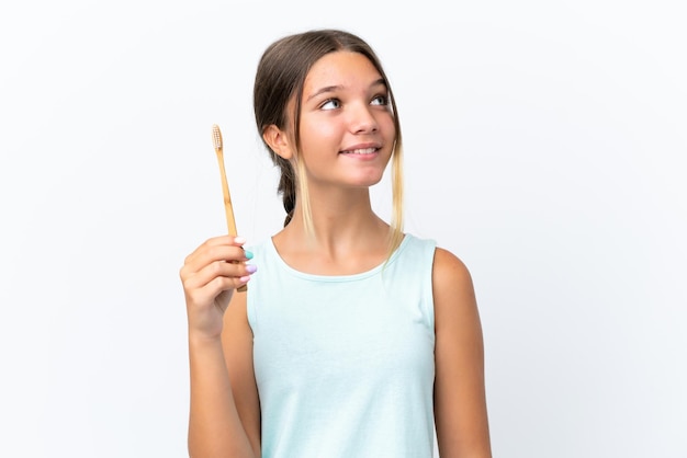 Little caucasian girl holding a toothbrush isolated on white background looking up while smiling
