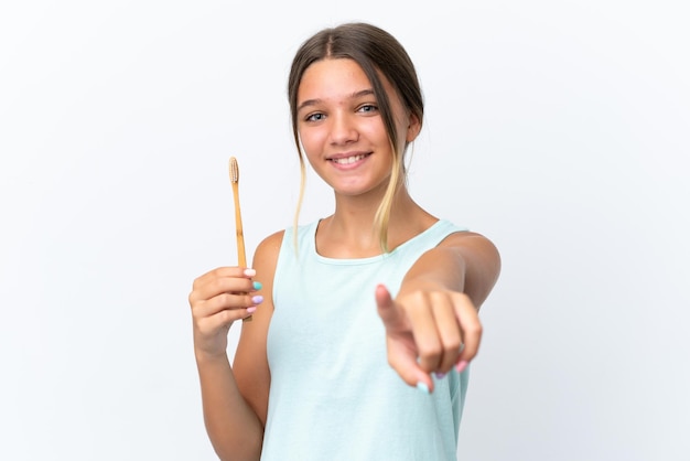 Little caucasian girl holding a toothbrush isolated on white background points finger at you with a confident expression