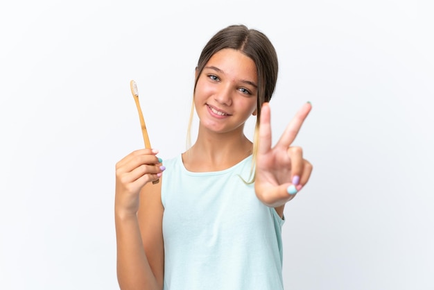 Little caucasian girl holding a toothbrush isolated on white background smiling and showing victory sign