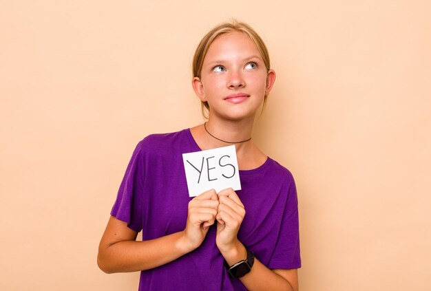 Little caucasian girl holding yes placard isolated on beige background