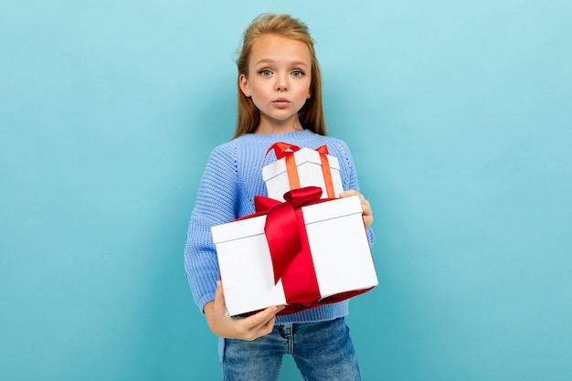 Little caucasian girl holds a white boxes with gifts and has no emotions isolated on blue