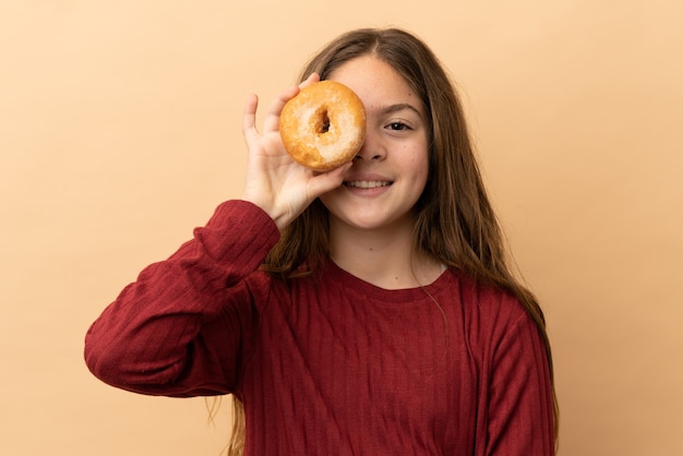 Little caucasian girl isolated on beige background holding a donut and happy