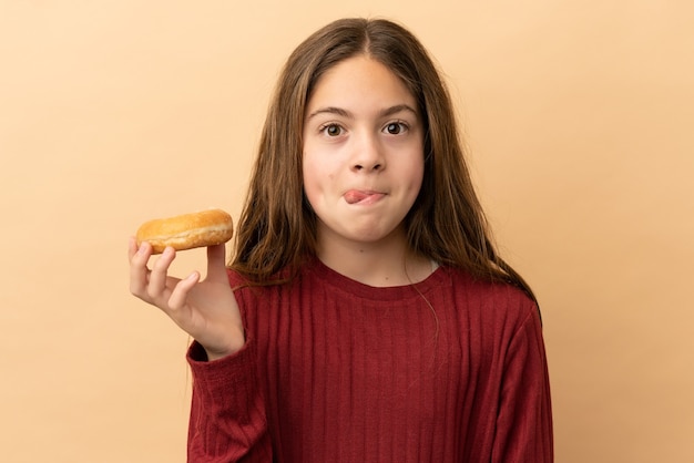 Little caucasian girl isolated on beige background holding a donut