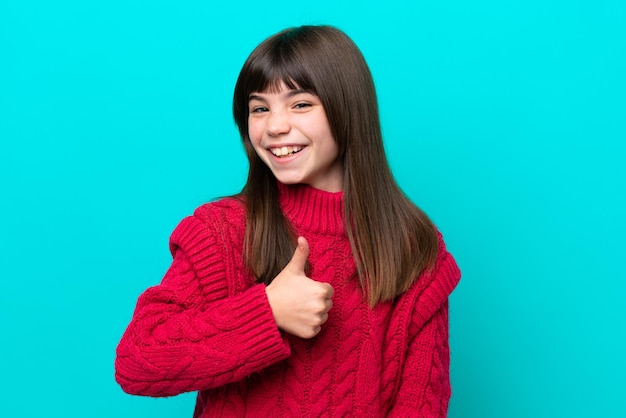 Little caucasian girl isolated on blue background giving a thumbs up gesture