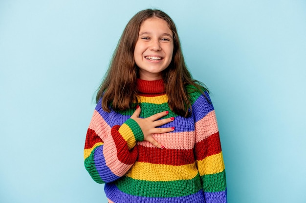 Little caucasian girl isolated on blue background laughs out loudly keeping hand on chest.