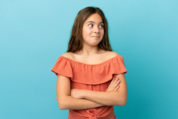 Little caucasian girl isolated on blue background making doubts gesture while lifting the shoulders