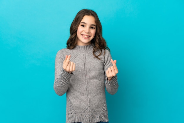 Little caucasian girl isolated on blue background making money gesture