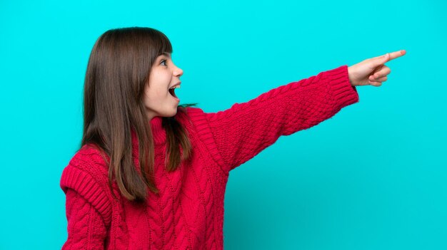 Little caucasian girl isolated on blue background pointing away