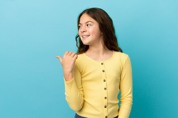 Little caucasian girl isolated on blue background pointing to the side to present a product