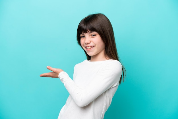 Little caucasian girl isolated on blue background presenting an idea while looking smiling towards