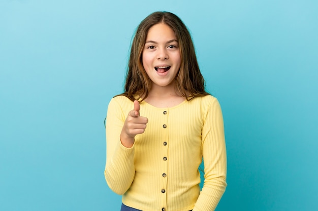 Little caucasian girl isolated on blue background surprised and pointing front