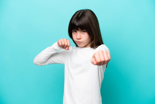 Little caucasian girl isolated on blue background with fighting gesture