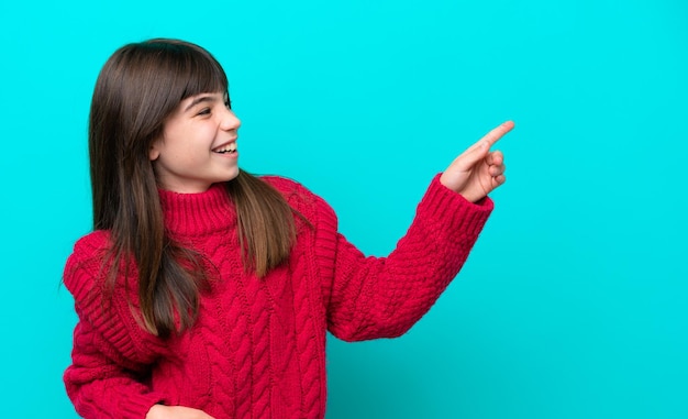 Маленькая кавказская девочка, изолированная на синем фоне, указывая пальцем в сторону и представляя продукт