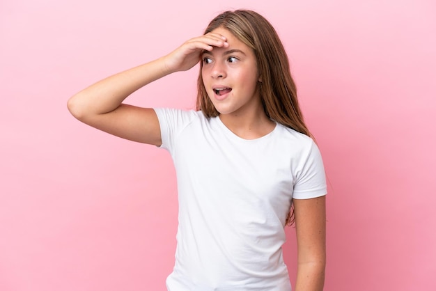 Little caucasian girl isolated on pink background doing surprise gesture while looking front