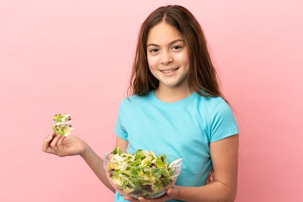 幸せな表情でサラダのボウルを保持しているピンクの背景に分離された白人の少女