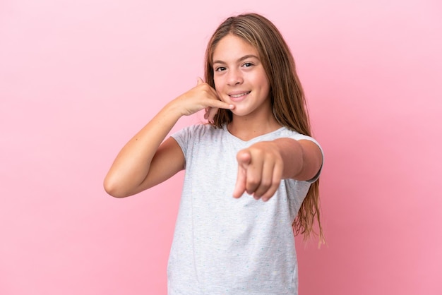 Little caucasian girl isolated on pink background making phone gesture and pointing front