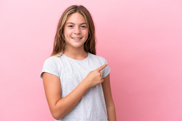 Little caucasian girl isolated on pink background pointing to the side to present a product