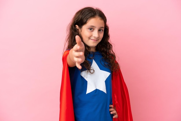 Little caucasian girl isolated on pink background in superhero costume and making a deal