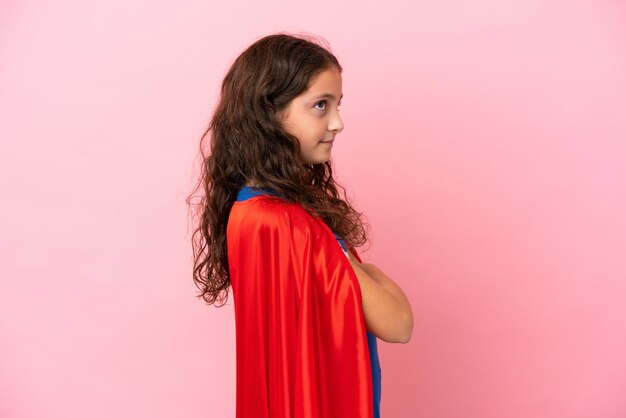 Little caucasian girl isolated on pink background in superhero costume with arms crossed