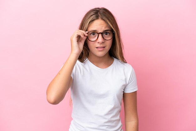 眼鏡と欲求不満の表情でピンクの背景に分離された小さな白人の女の子