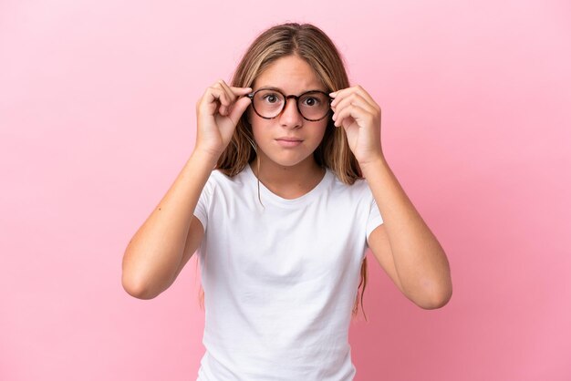 眼鏡と欲求不満の表情でピンクの背景に分離された小さな白人の女の子