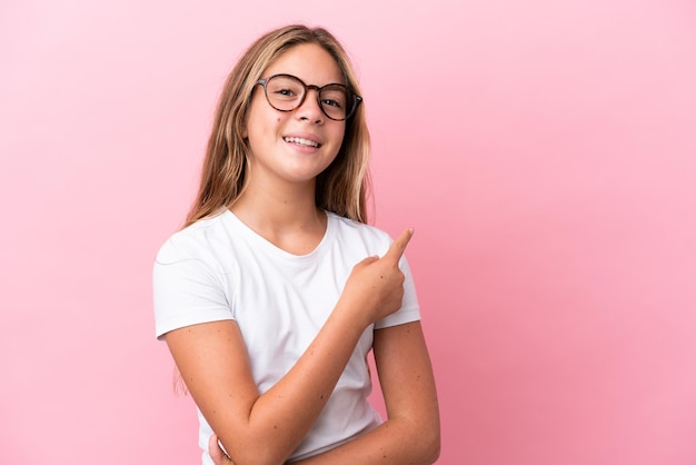 Little caucasian girl isolated on pink background With glasses and pointing side