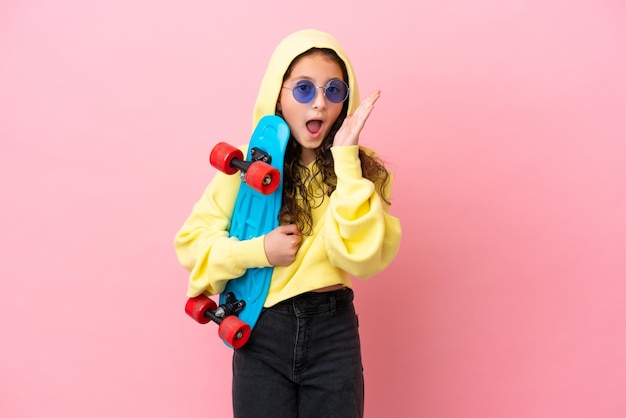Little caucasian girl isolated on pink background with a skate and doing surprise gesture