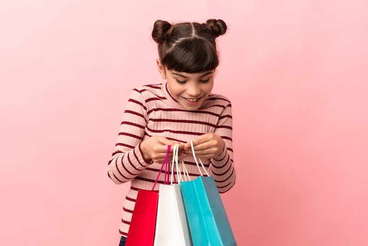 Photo little caucasian girl isolated on pink holding shopping bags and looking inside it