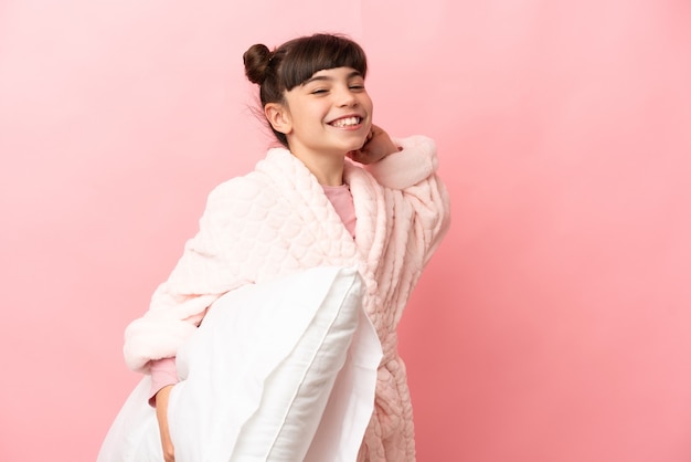 Little caucasian girl isolated on pink in pajamas and holding a pillow and yawning