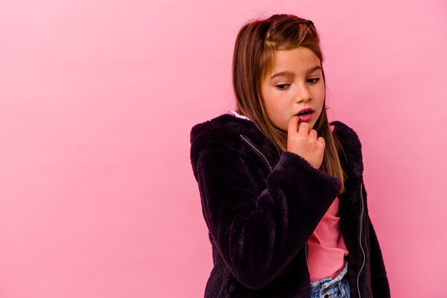 Little caucasian girl isolated on pink wall  relaxed thinking about something looking at a copy space.