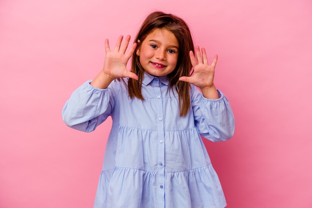 Piccola ragazza caucasica isolata sulla parete rosa che mostra il numero dieci con le mani.