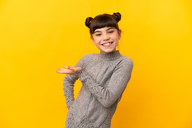 Little caucasian girl isolated presenting an idea while looking smiling towards