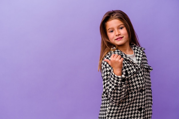 Little caucasian girl isolated on purple Little caucasian girl isolated on purple points with thumb finger away, laughing and carefree.