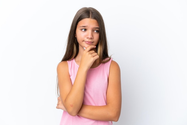 Little caucasian girl isolated on white background having doubts and thinking