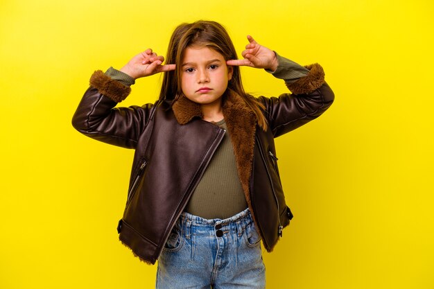 Little caucasian girl isolated on yellow background focused on a task, keeping forefingers pointing head.