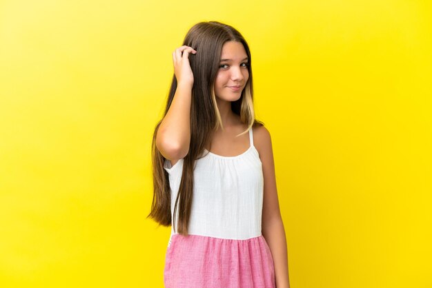 Little caucasian girl isolated on yellow background having doubts