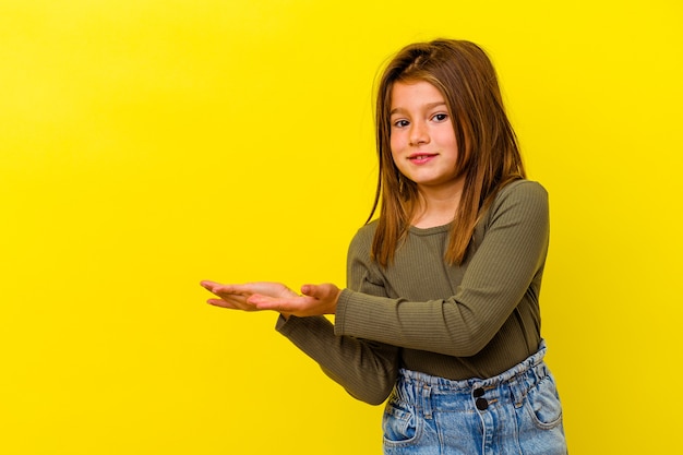 Little caucasian girl isolated on yellow background holding a copy space on a palm