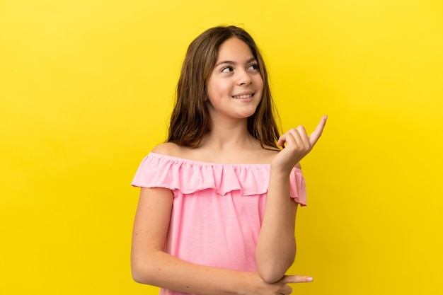 Little caucasian girl isolated on yellow background pointing up a great idea