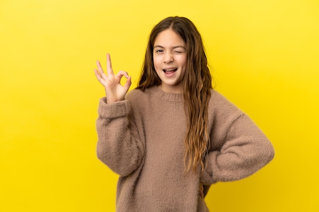 손가락으로 확인 표시를 보여주는 노란색 배경에 고립 된 어린 백인 소녀